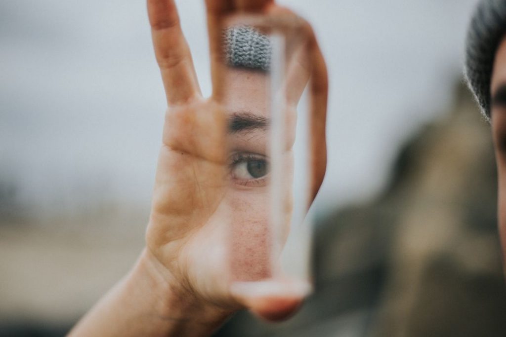 Eine Person hält eine Scherbe in der Hand, in der sich ihr Auge spiegelt