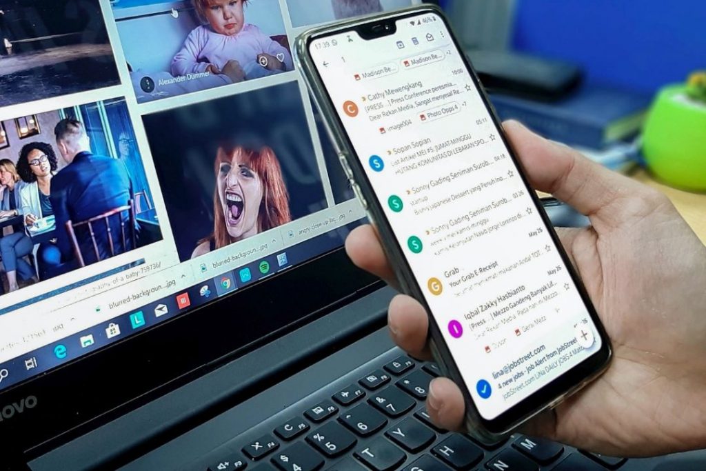 Eine Person hält ein Smartphone vor einem Laptop