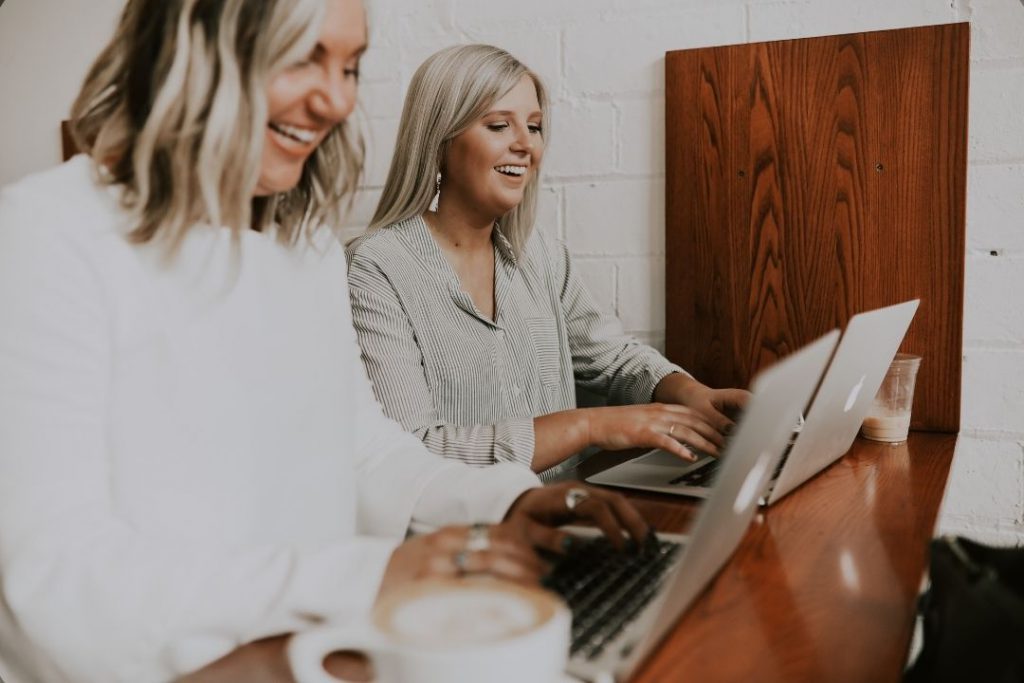 Zwei Frauen arbeiten an je einem Computer und lachen